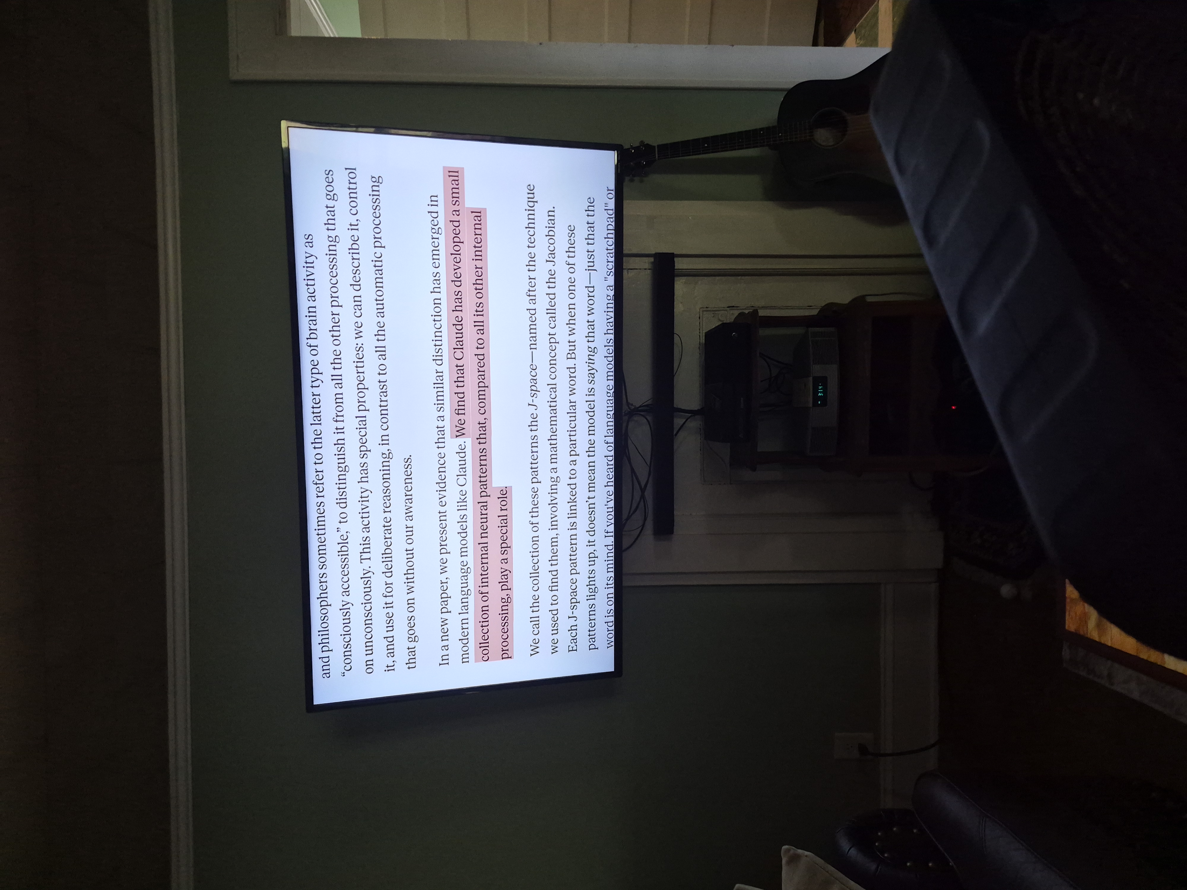 A television on a living-room wall showing Anthropic's research on Claude's internal J-space, a passage highlighted in pink